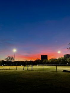 the sun is setting over a soccer field with lights in the distance and trees on either side