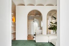 a living room with white walls and green carpeted flooring in front of an arched doorway