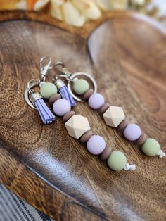 two key chains with beads and tassels sitting on a wooden table next to flowers