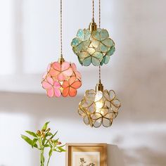 three colorful lights hanging from the ceiling above a vase with flowers in it on a table