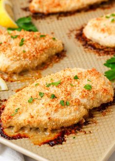 some food that is sitting on a baking sheet with lemon wedges and parmesan cheese