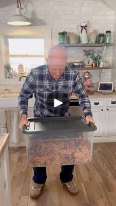 a man standing in a kitchen holding a box filled with food