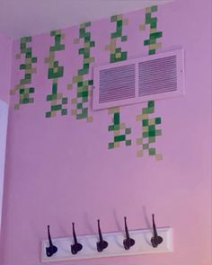 a pink wall with green squares on it and four coat hooks hanging from the ceiling