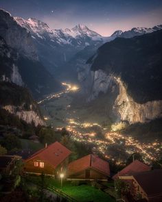 the mountains are lit up at night with lights shining on them and houses in the foreground