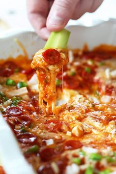 a person dipping some kind of vegetable into a casserole dish with cheese and tomato sauce