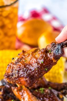 a person is holding up some ribs with sauce on it and corn in the background