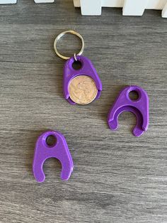 three purple keychains are sitting next to a penny on a wooden table with white radiator