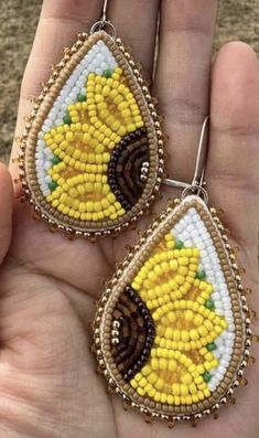 two yellow and white beaded sunflowers are hanging from the side of a pair of earrings