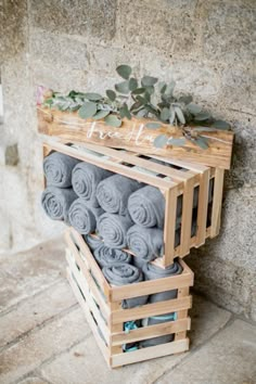 a wooden crate filled with rolled up gray towels next to a stone wall and greenery