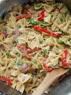 a pan filled with pasta and peas on top of a stove next to a wooden spoon