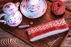 a table topped with yarn and other items on top of a wooden tray next to a pair of scissors