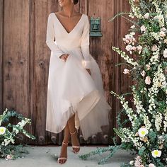 a woman standing in front of a wooden door wearing a white dress with long sleeves