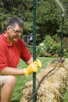 a man kneeling down next to a pile of hay and holding a pair of yellow gloves