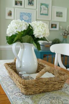 a white vase filled with flowers sitting on top of a table next to a wicker basket