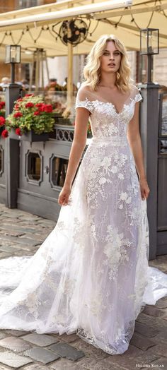 a woman in a white wedding dress standing on a brick walkway with her hands behind her back