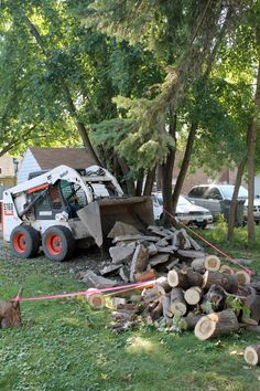 a tractor is parked in front of a pile of firewood and some cars behind it