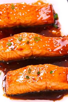 three salmon fillets on a white plate covered in sauce and garnished with green onions