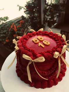 a red cake decorated with pretzels and ribbons on a table outside in the sun