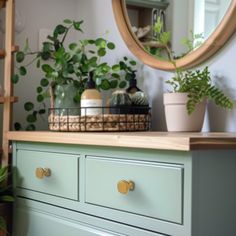 a green dresser with some plants on top of it and a round mirror above it