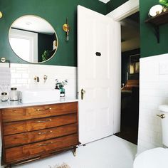 a white toilet sitting next to a bathroom sink under a round mirror on a wall