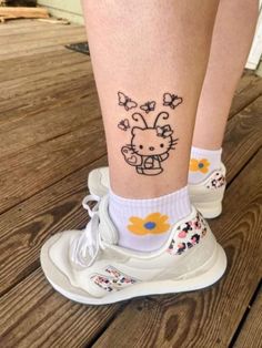 a hello kitty tattoo on the leg of a person wearing white sneakers with yellow flowers