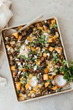 a casserole dish with vegetables and feta cheese on top, next to a spoon