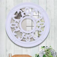 a white circular mirror hanging on the wall next to a vase with flowers in it