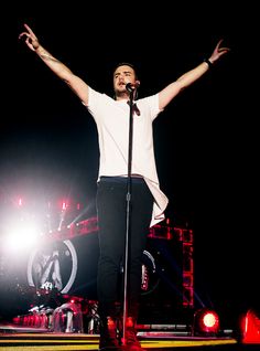 a man standing on top of a stage holding his arms up in the air while singing into a microphone