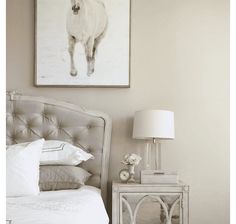 a white horse is hanging on the wall above a bed with pillows and a lamp