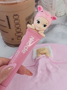 a hand holding a tube of toothpaste with a baby doll on it and a cup of coffee in the background