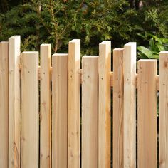 a close up of a wooden fence with trees in the back ground and bushes behind it