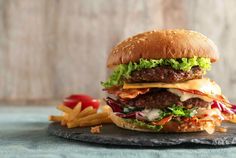 a cheeseburger with lettuce, tomato and onion on a slate platter