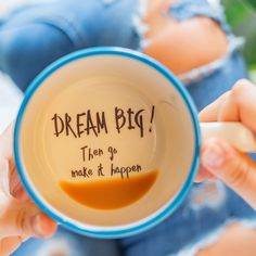 a person holding a coffee cup with writing on the inside and bottom that says, dream big then go make it happen