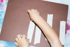 a child is cutting out strips of paper on a piece of brown paper with white tape