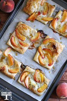 several pieces of fruit pizza on a baking sheet with peaches and other fruits around them