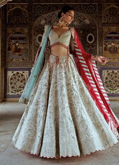 Featuring the stunning Silver Colour Tissue Embroidered Lehenga is a timeless masterpiece crafted for those who value elegance and craftsmanship. The silver lehenga, made from a luxurious tissue, is adorned with intricate silver dori embroidery, complemented by dabka, sequins, and a delicate arrangement of red and aqua beads. Its shimmering tissue fabric exudes a regal charm. Paired with a beautifully embellished blouse, it features intricate red tassel beads along the waist and sleeve edges for a touch of playfulness. Completed with a choice of aqua tulle or red dupatta, that adds a sophisticated contrast to the lehenga’s design. This lehenga is the ultimate choice for the modern bride or bride-to-be seeking to make a memorable statement at her special event. Composition : Lehenga, Blouse