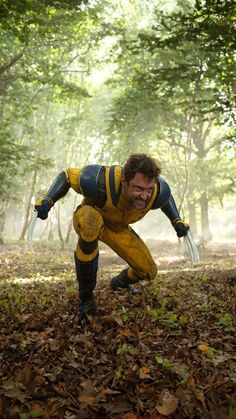 a man dressed as wolverine in the woods with leaves on the ground and trees behind him