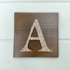 a wooden sign with the letter a made out of yarn on it's side