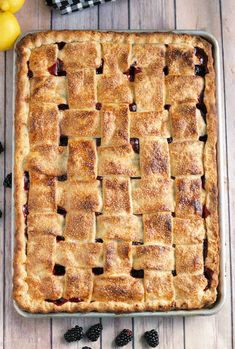 a pie sitting on top of a wooden table next to lemons and blackberries