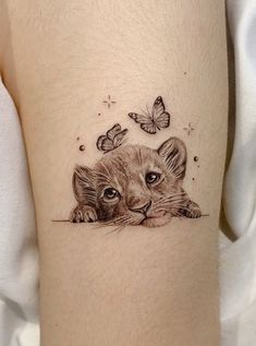 a small tiger cub with butterflies on its head and behind it is a butterfly tattoo