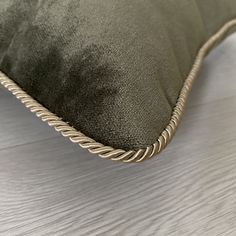 a close up view of a green pillow on a white wood floor with the corded edge