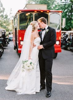 a bride and groom kissing in front of a red bus