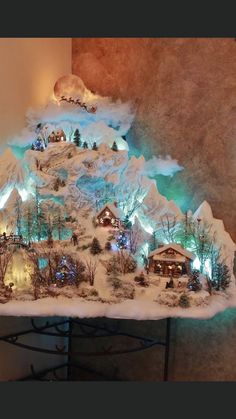 a lighted christmas village on top of a table with trees and houses in the snow