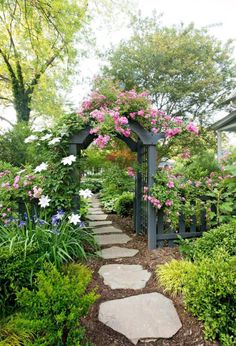 a stone path leads to a garden with pink and white flowers on the arbors