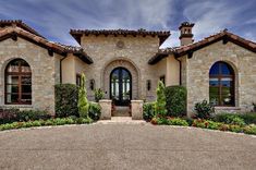 a large stone house with lots of windows and plants on the front lawn, along with an entry way