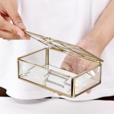 a person is holding a glass jewelry box in their hands, with the lid open