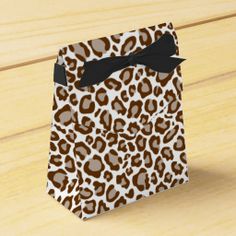 a brown and white leopard print paper bag with a black bow on the top, sitting on a wooden surface