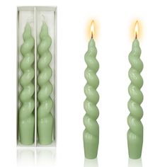 two green candles sitting next to each other in front of a white box with one candle lit