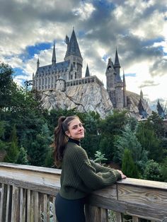 a woman leaning on a wooden fence in front of hogwarts castle at the wizarding world