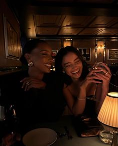 two women sitting at a table with wine glasses in their hands and one woman smiling